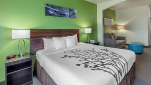 Una habitación de hotel con cama, mesita de noche, lámpara y un cuadro en la pared.