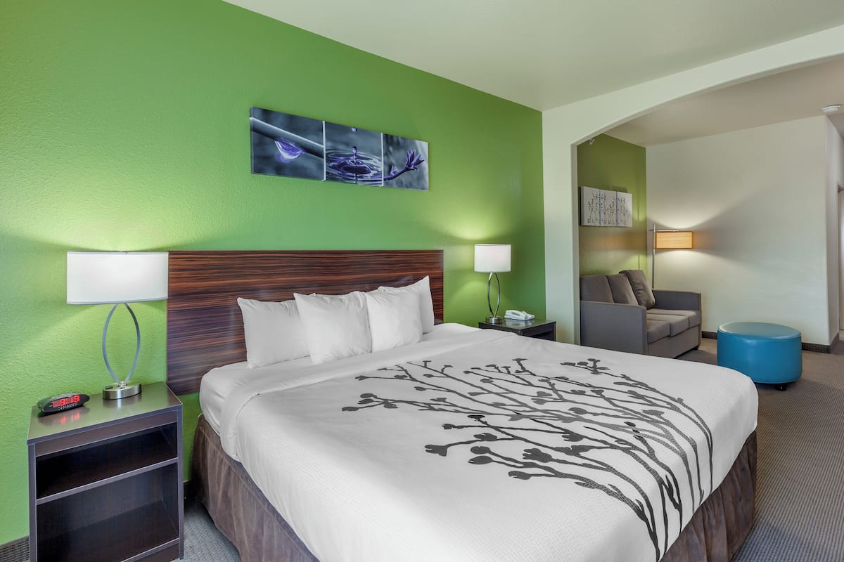 A hotel room with a bed, nightstand, lamp, and a painting on the wall.