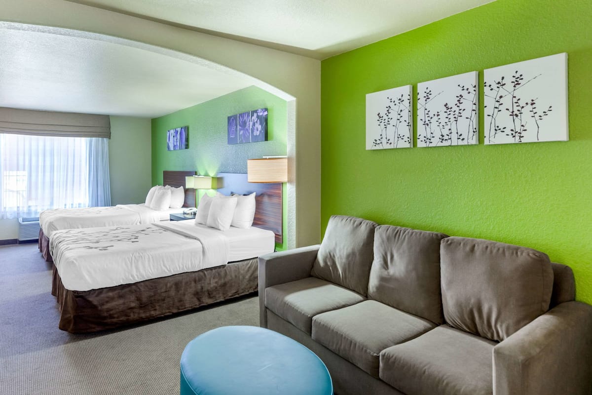 A hotel room with a large bed, a sofa, and a blue ottoman. There are three wall art pieces above the sofa.