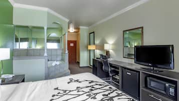 A hotel room with a bed, a desk, a television, a mirror, and a bathroom with a shower and toilet.