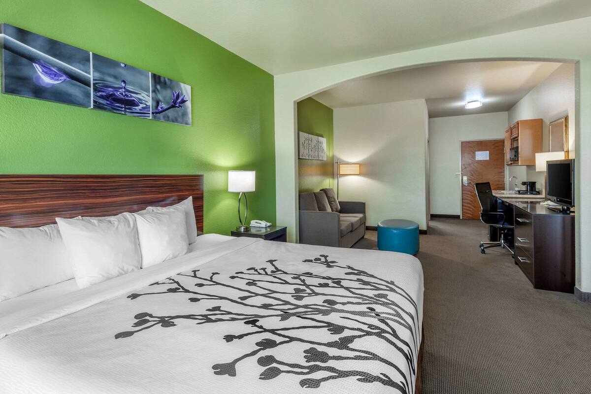 A hotel room with a large bed, a desk, and a kitchenette.