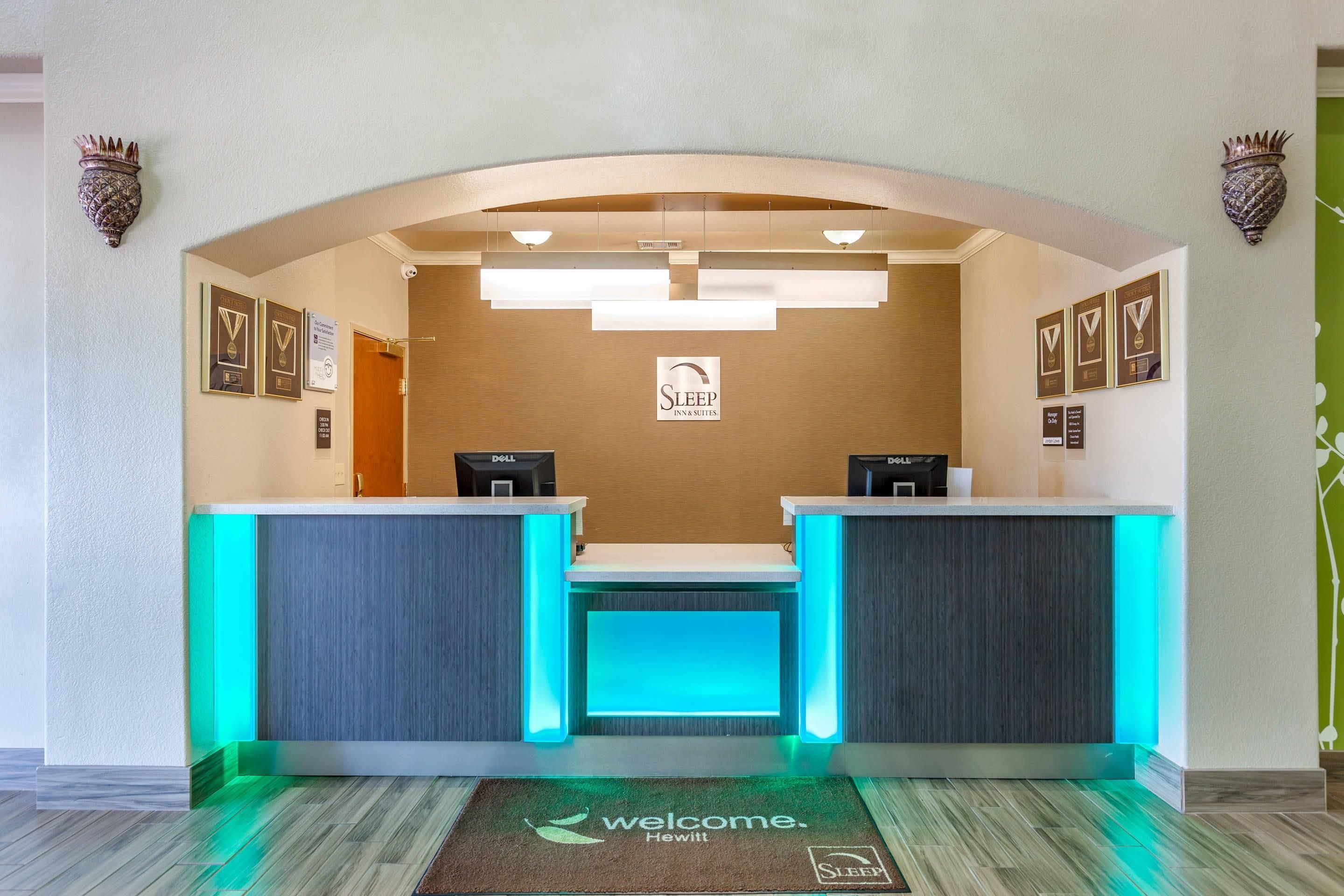 A reception desk with a 'Welcome' mat, framed awards, and a sign for 'Sleep Inn & Suites.'
