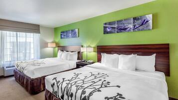 A hotel room with two beds, a green accent wall, and artwork above the beds.