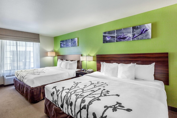 A hotel room with two beds, a green accent wall, and artwork above the beds. - Sleep Inn & Suites Hewitt - South Waco (Hewitt)