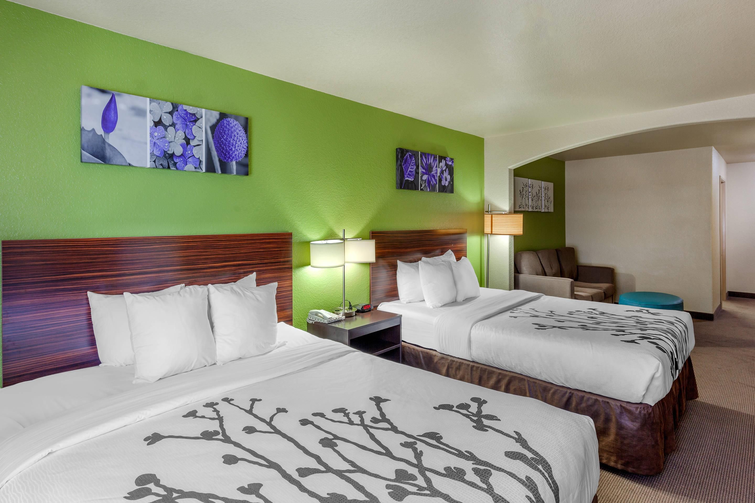 Een hotelkamer met twee bedden, een bureau, een stoel en kunstwerken aan de wanden.
