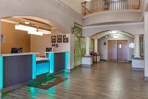 A hotel reception area with a reception desk, a digital display, framed awards on the wall, and a staircase leading to an upper level. - Sleep Inn & Suites Hewitt - South Waco (Hewitt)
