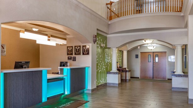 A hotel reception area with a modern design, including a reception desk, framed awards, and a staircase leading to an upper level. - Sleep Inn & Suites Hewitt - South Waco (Hewitt)