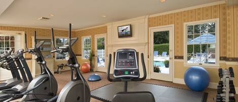 A gym with exercise equipment, a digital display, and a view of a pool through a door.
