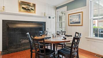 A dining area with a fireplace, wooden chairs, a round table, and a framed picture on the wall.