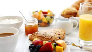 Mesa de café da manhã com uma travessa de frutas, um copo de suco de laranja, um pote de geleia e uma tigela de cereal.