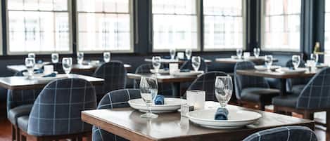 A restaurant with tables set for dining, featuring plaid chairs and large windows.