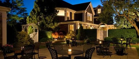 A large house with a patio area featuring outdoor furniture and a well-lit garden.