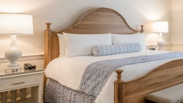 A neatly made bed with a wooden headboard, white bedding, and a patterned throw. There are bedside tables with lamps and a small drawer.