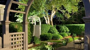 A garden with a pergola structure, a pathway, and a seating area.