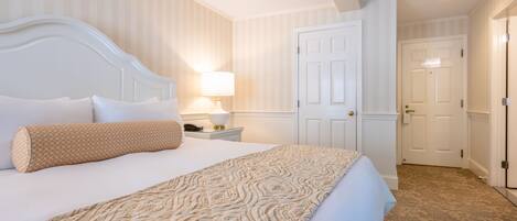 A hotel room with a large bed, a bedside table with a lamp, a door, and a carpeted floor.