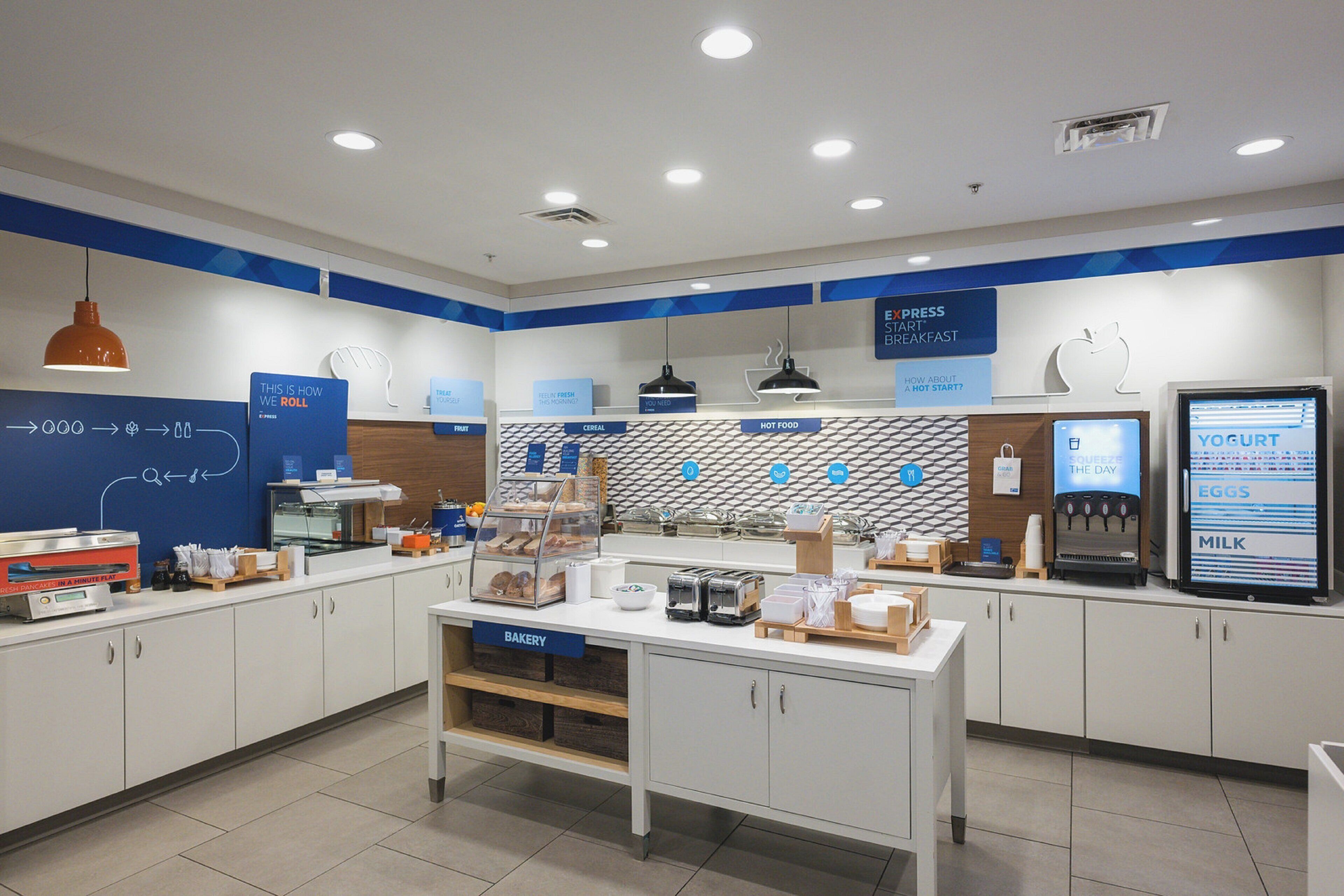 A modern breakfast area with a bakery section, a yogurt machine, and a display of hot food options.