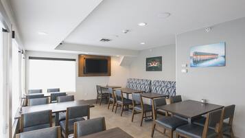 A modern dining area with multiple tables and chairs, a large window, and a wall-mounted TV.