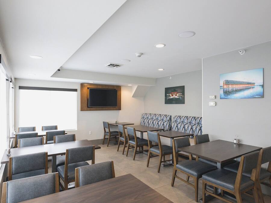 A modern dining area with multiple tables and chairs, a large window, and a wall-mounted TV.