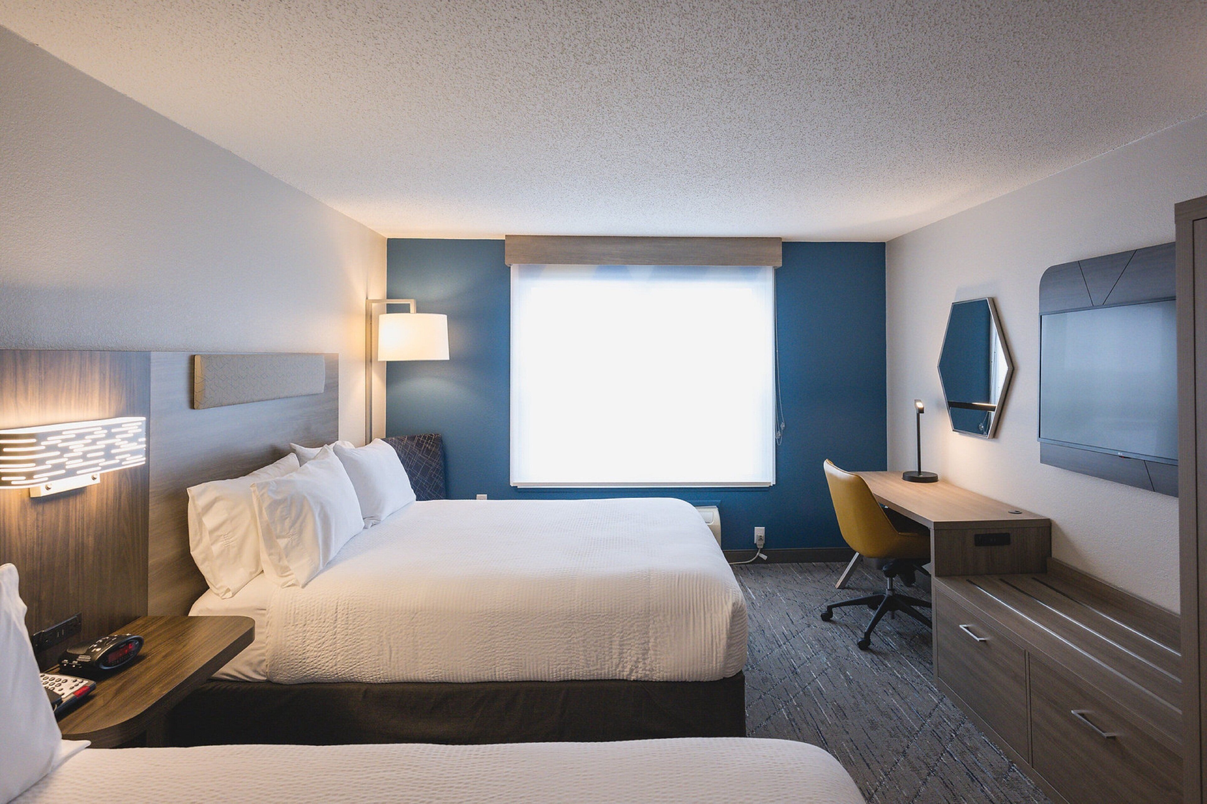 A hotel room with a large bed, a desk, a chair, a TV, and a window.