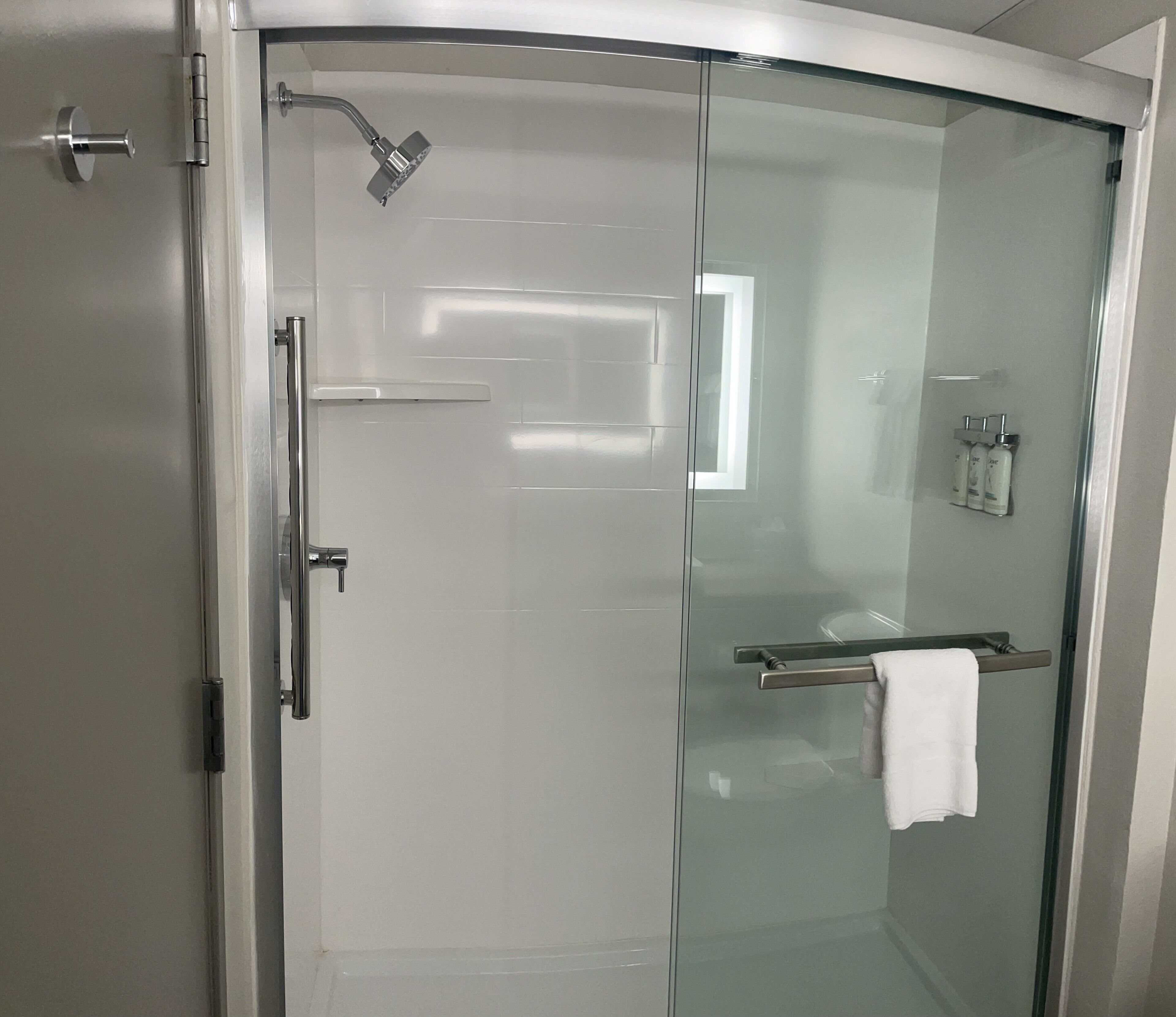 A modern bathroom with a glass-enclosed shower, a towel rack, and a small shelf with toiletries.