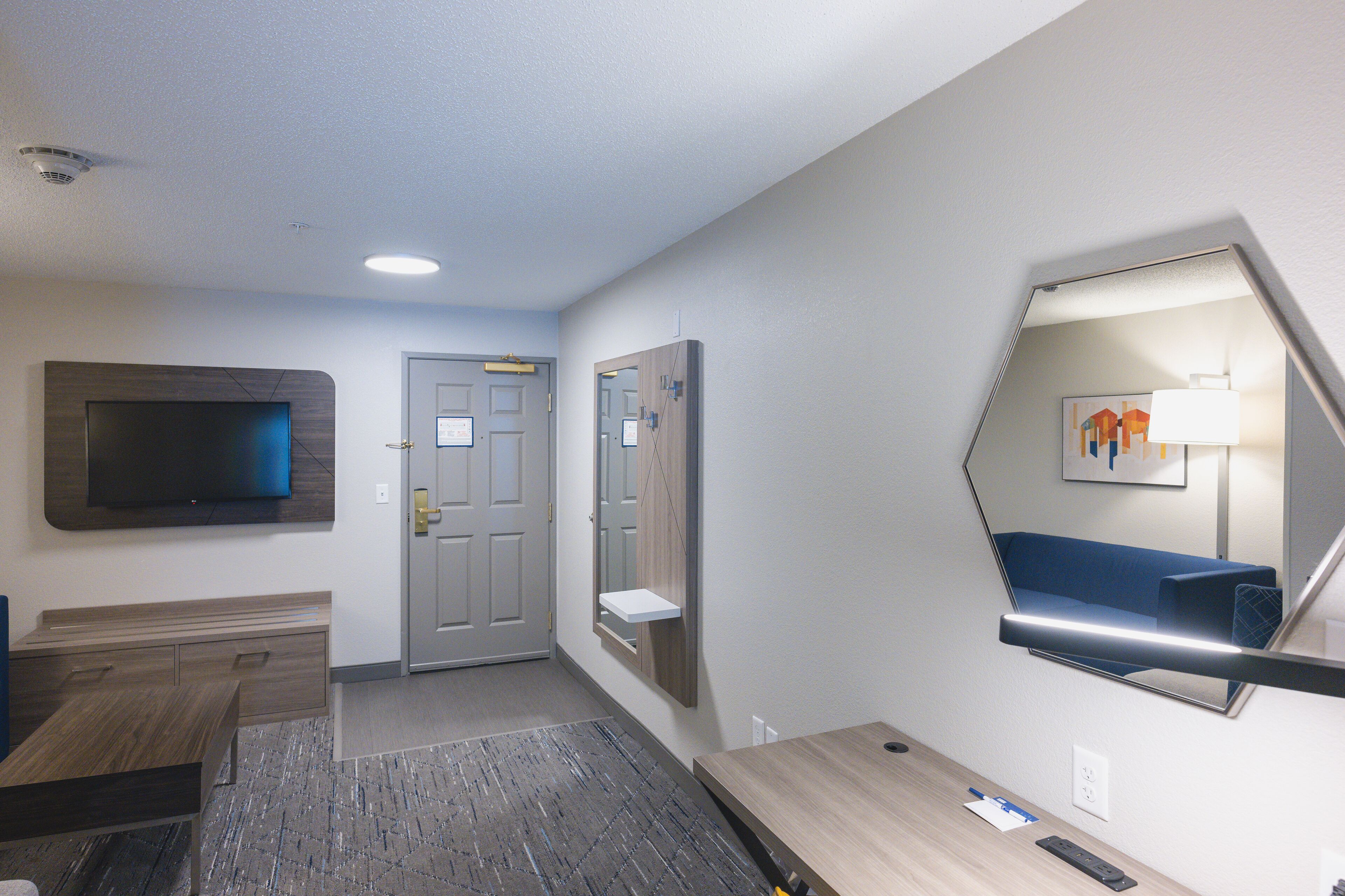 A hotel room with a flat-screen TV, a desk, a mirror, and a door.