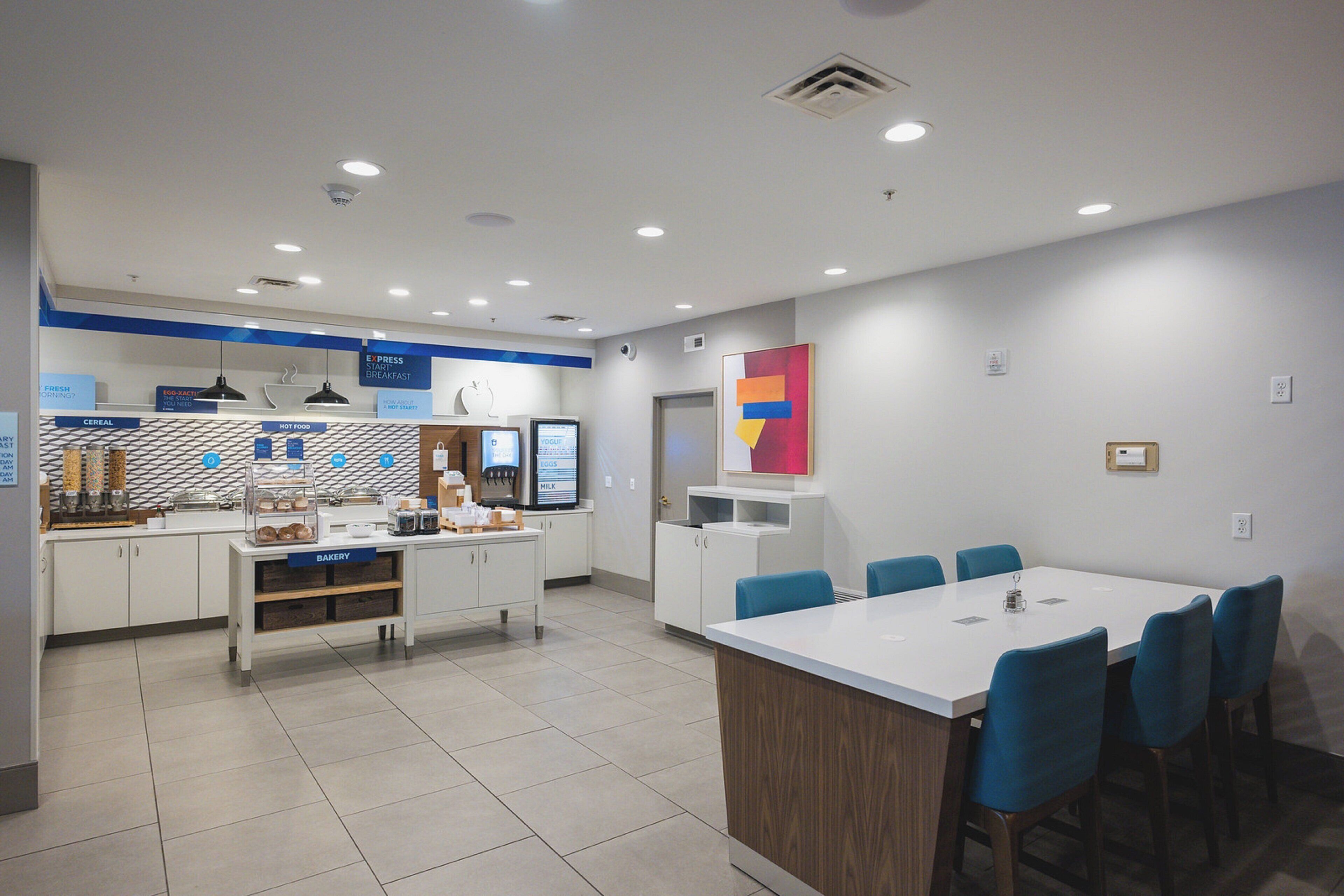 A modern breakfast area with a counter displaying various food items and a digital menu board.