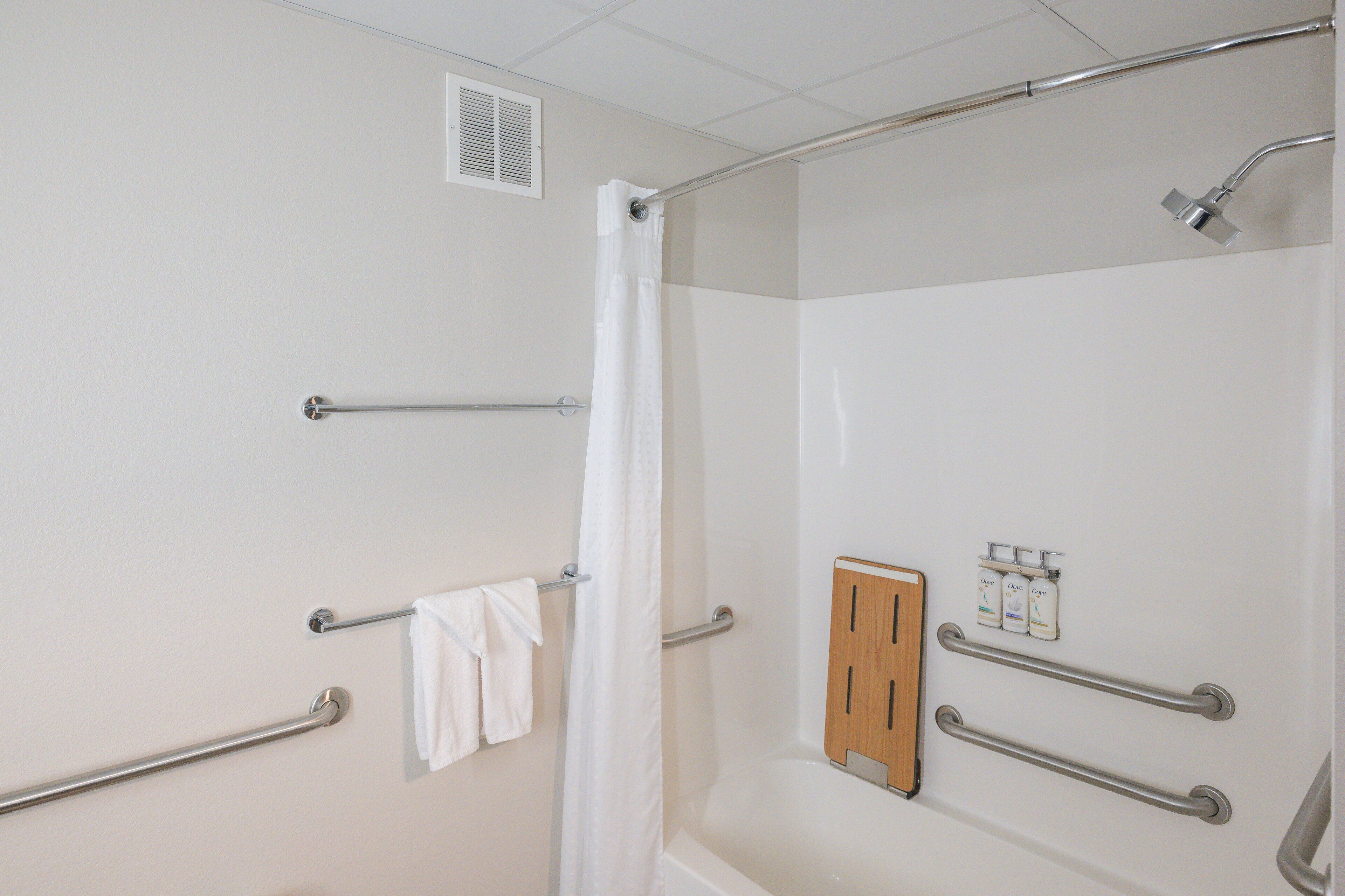 A bathroom with a shower, grab bars, a towel rack, and a soap dispenser.