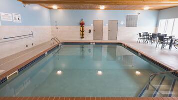 An indoor swimming pool with a 3ft depth sign, a lifeguard stand, and a seating area with tables and chairs.