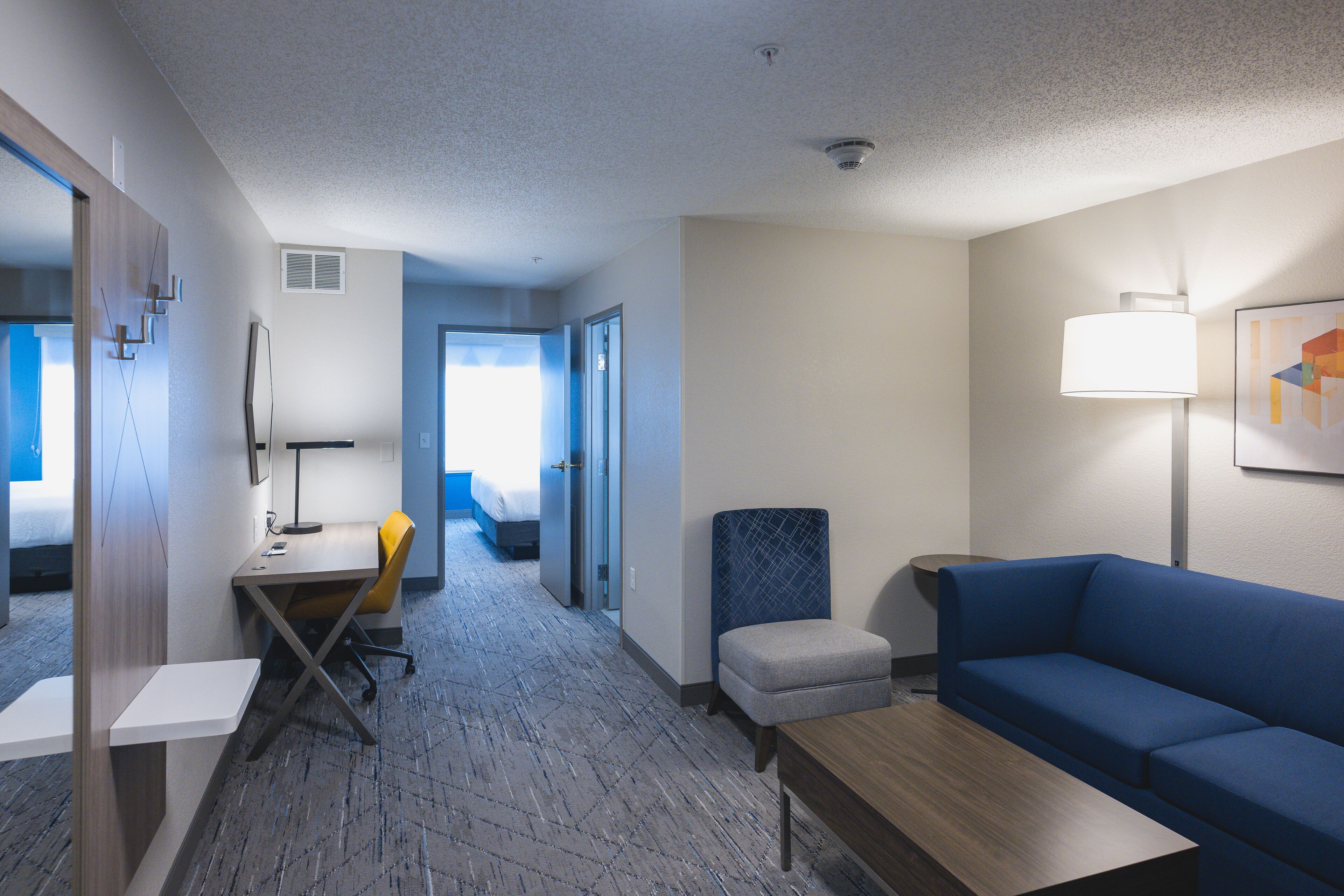Habitación de hotel con escritorio, silla, sofá y lámpara.