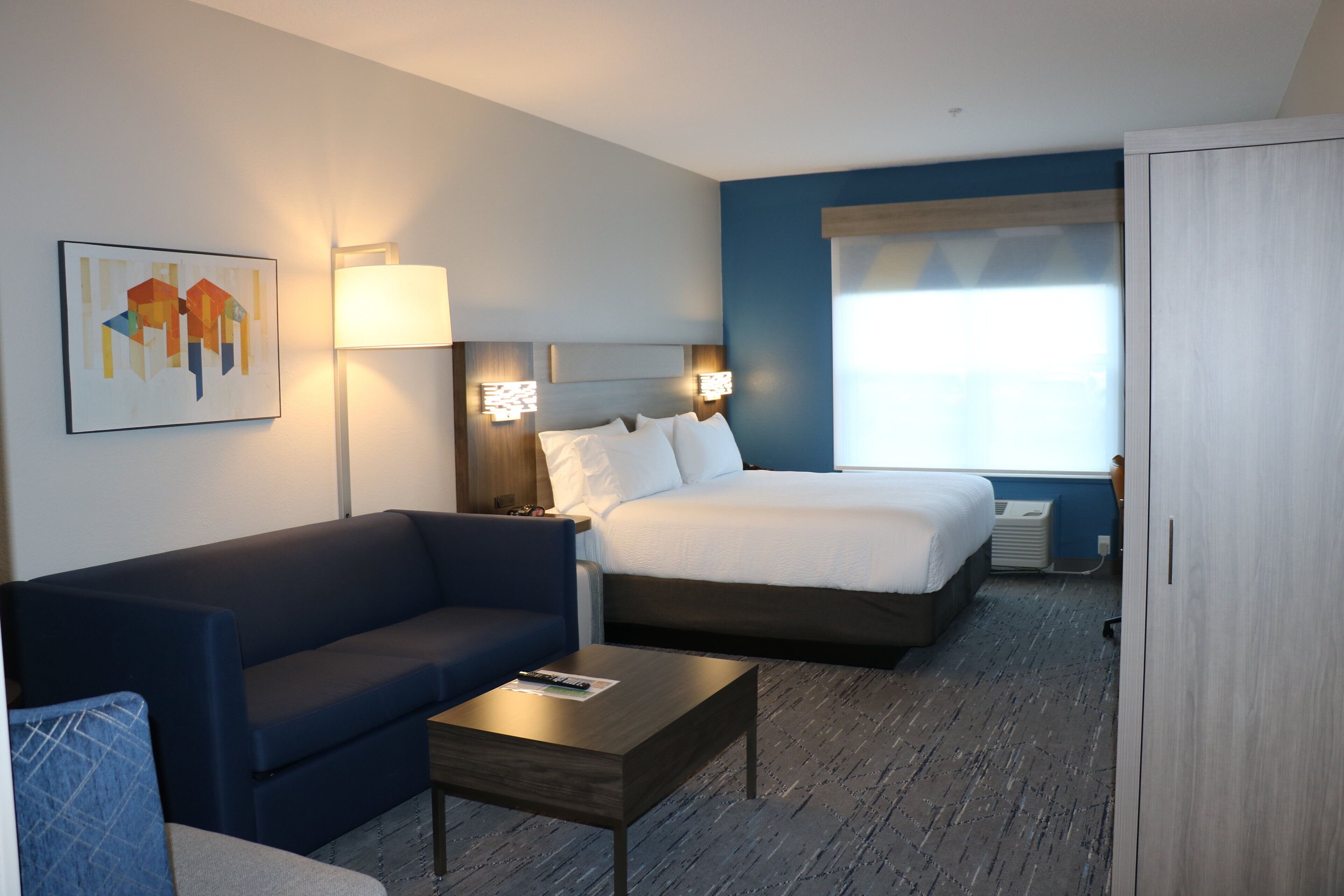 A hotel room with a bed, a sofa, a coffee table, and a painting on the wall.