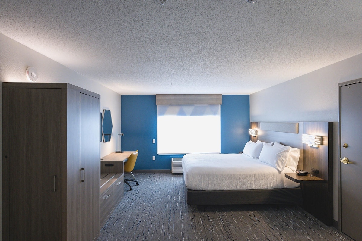 A hotel room with a bed, desk, chair, and a window with blinds.