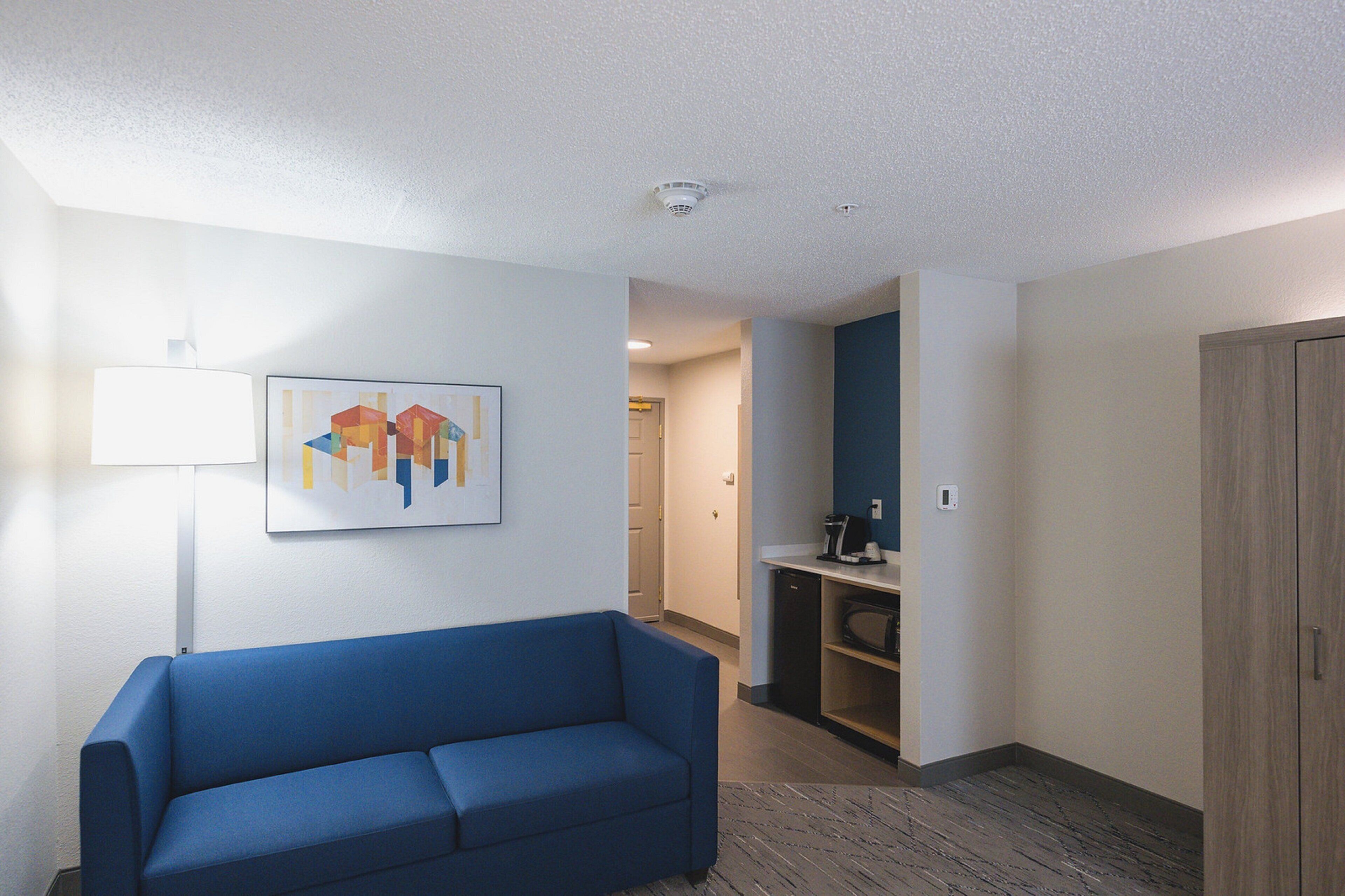 A hotel room with a blue sofa, a painting on the wall, a microwave, and a wooden cabinet.