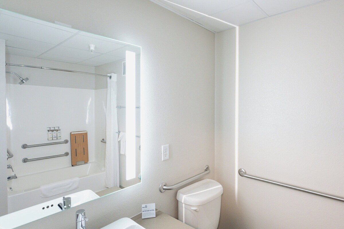 Une salle de bain moderne avec un grand miroir, une baignoire, des toilettes et un lavabo.