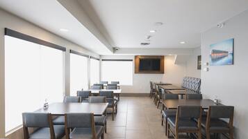 A conference room with multiple tables and chairs, large windows, a mounted television, and a painting on the wall.