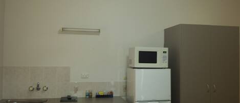 A compact kitchen with a microwave on top of a refrigerator, a sink, and a dining table with chairs.