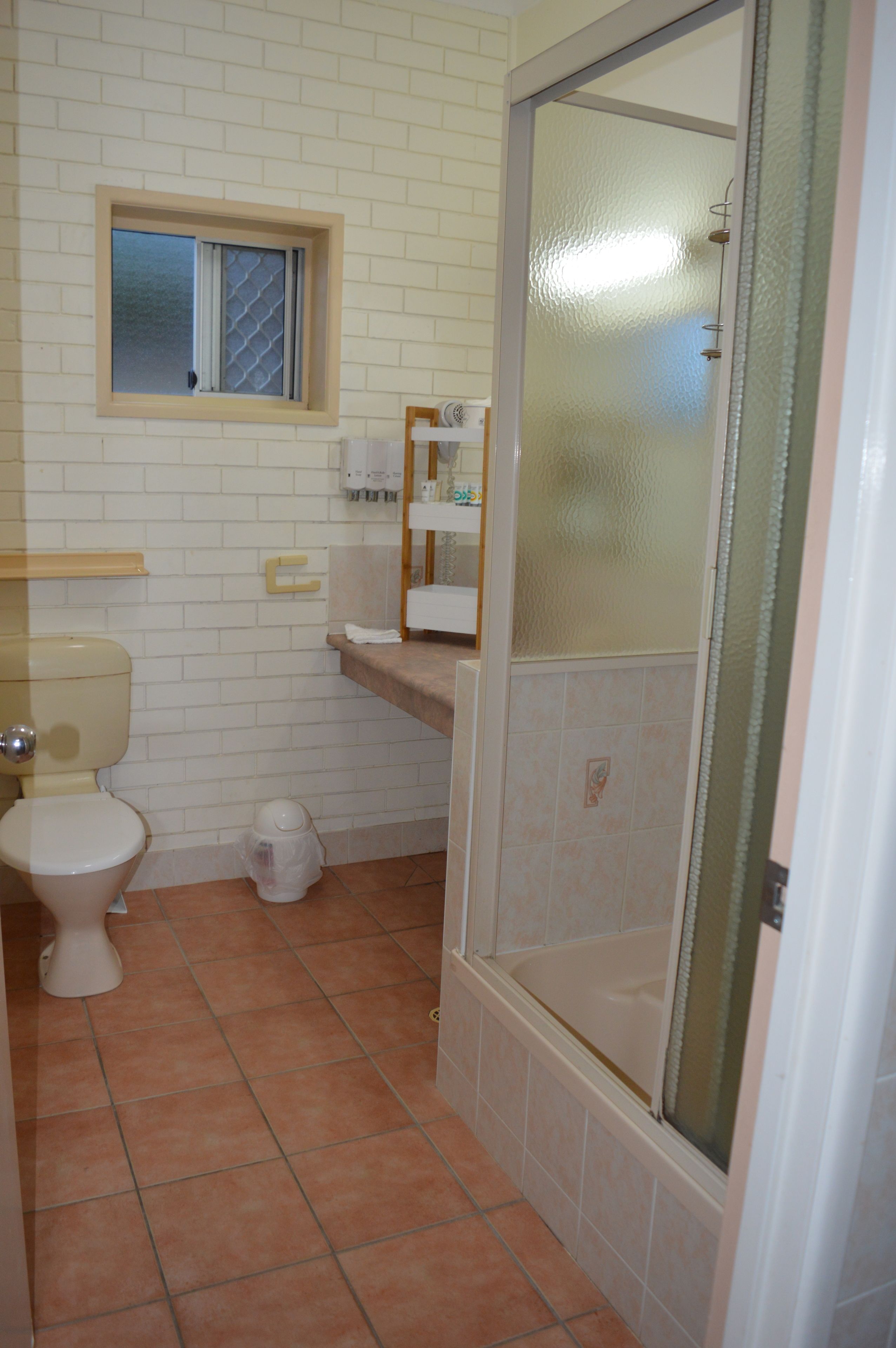 Un baño con inodoro, lavamanos, ducha con puertas de vidrio satinado y una ventana sobre el inodoro.