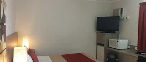 A hotel room with a bed, a desk with a computer, a television, and a microwave.