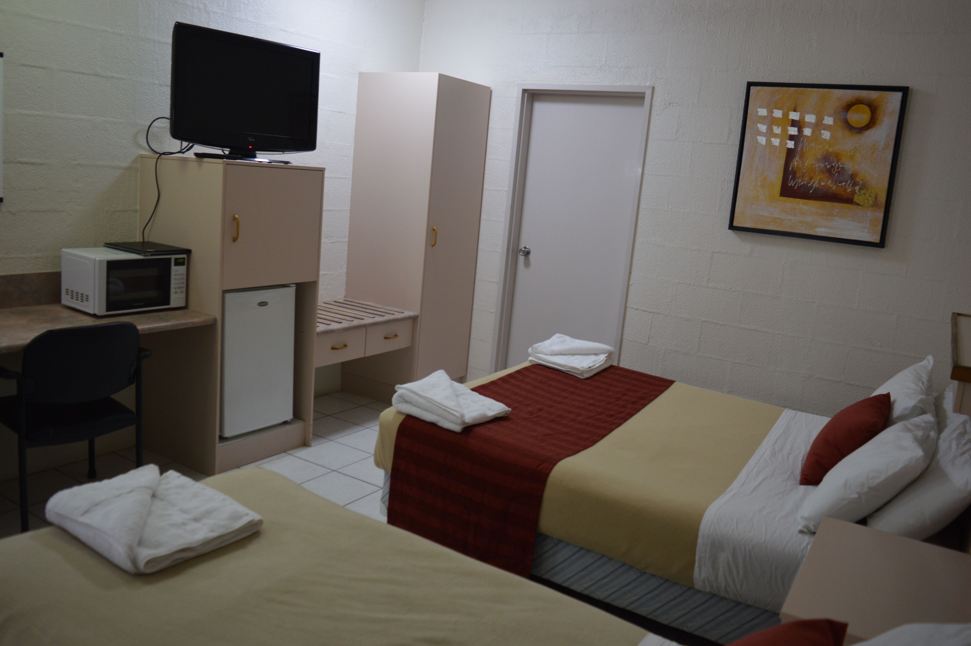Habitación de hotel con cama, escritorio con computadora y microondas, refrigerador pequeño y televisor en un mueble.