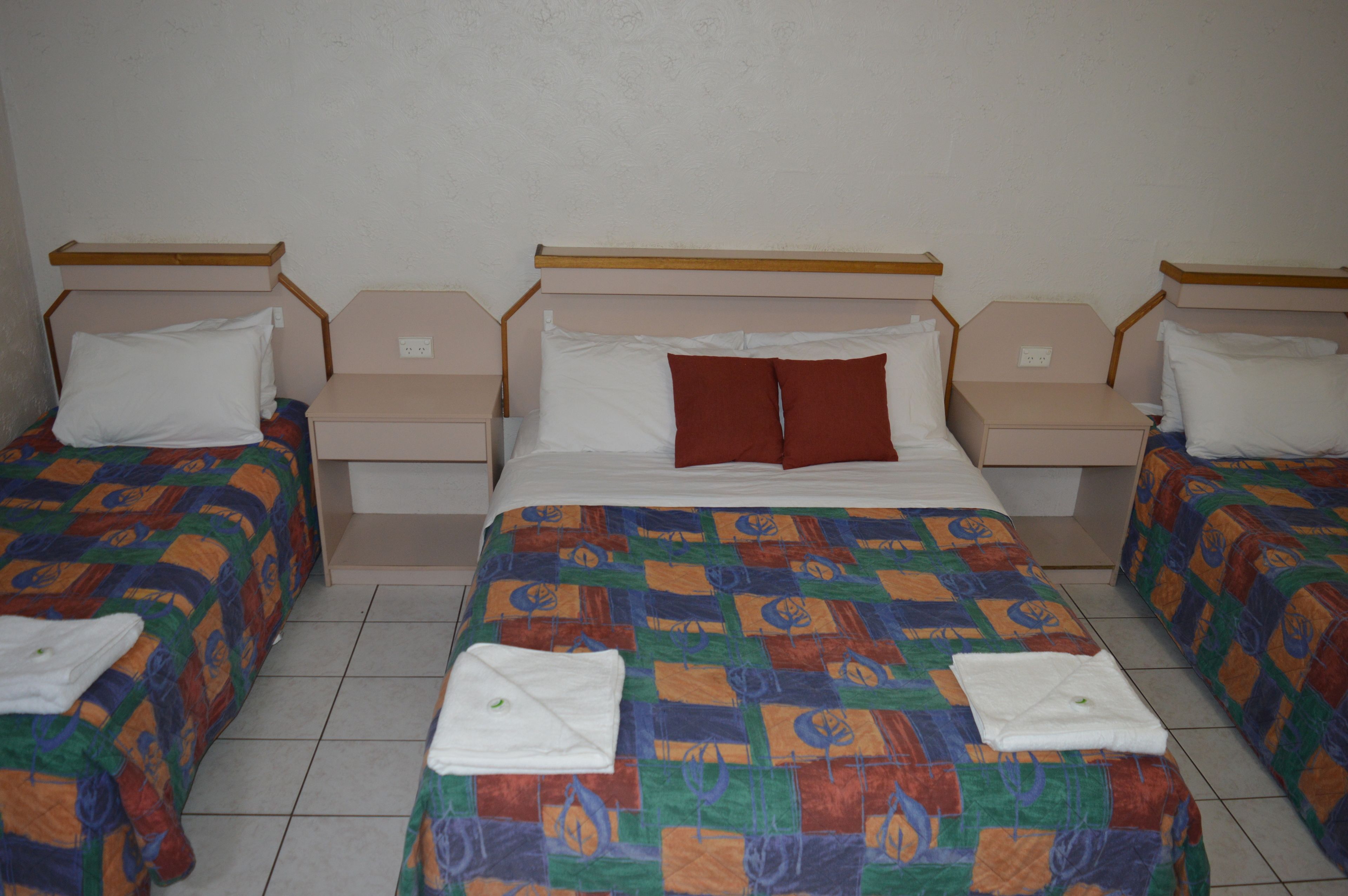 A hotel room with a large bed, two smaller beds, and a nightstand with a lamp.