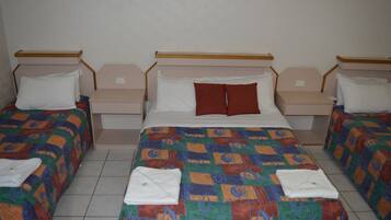 A hotel room with a large bed, two smaller beds, and a nightstand with a lamp.
