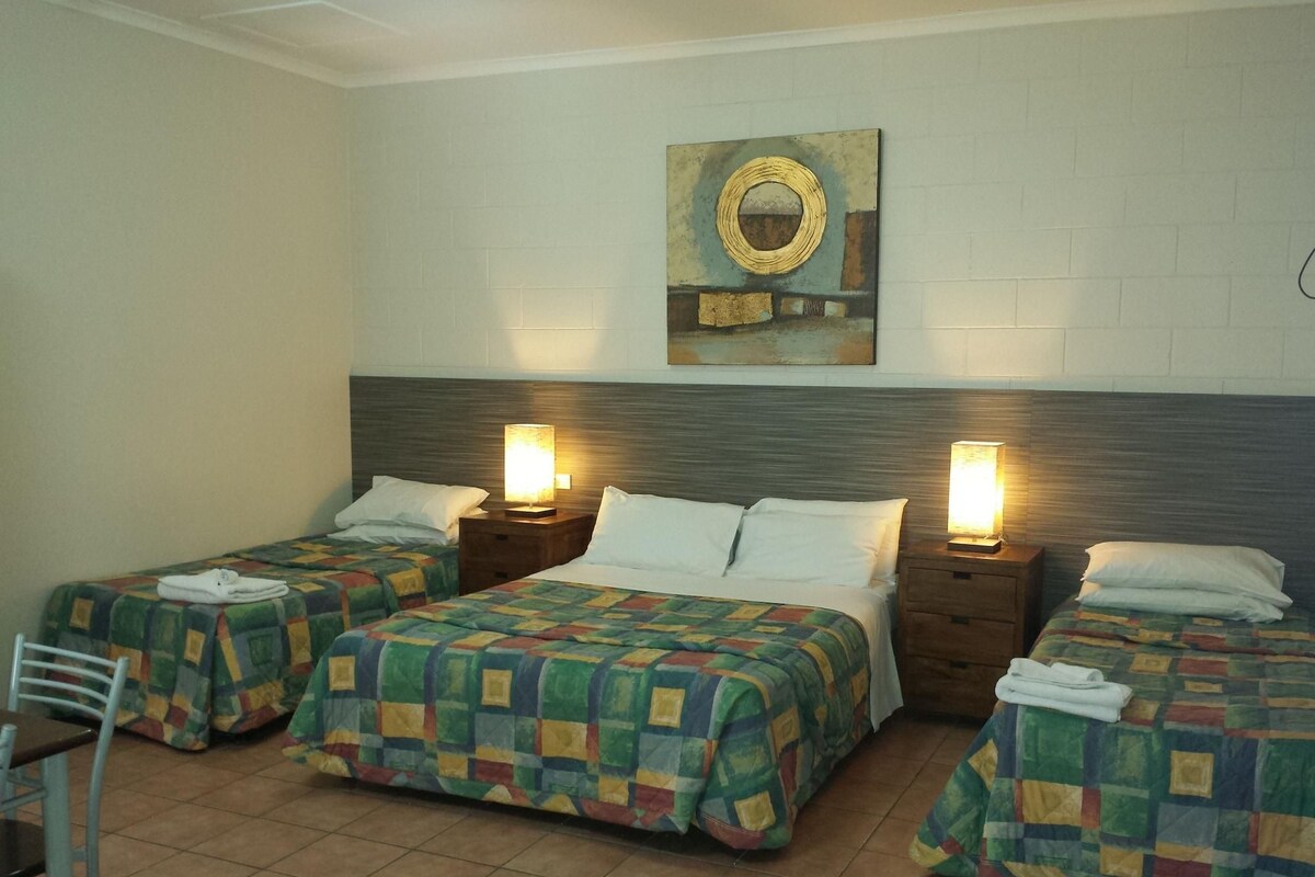 A hotel room with two single beds, a double bed, a chair, and a table.