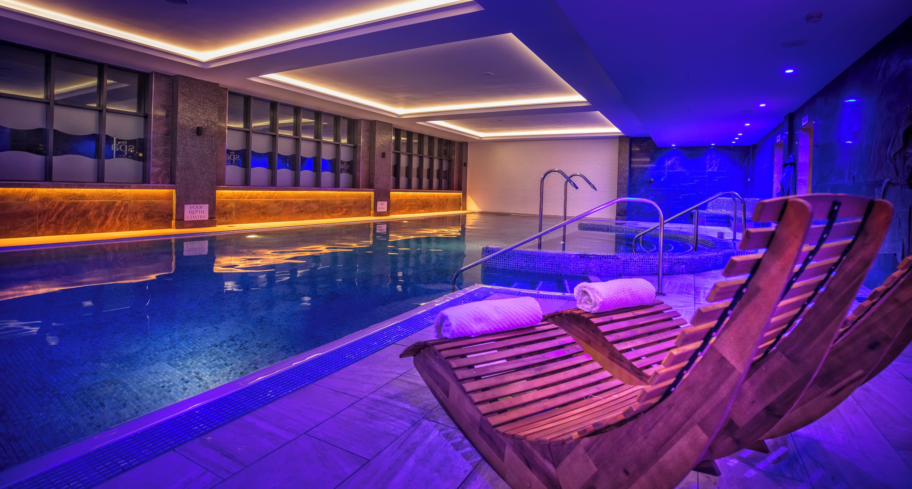 A swimming pool area with wooden loungers, a hot tub, and a reception desk.