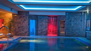 A modern indoor pool area with a glass barrier, marble walls, and a red-lit entrance. - Quay Hotel and Spa (Conwy)