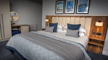 A hotel room with a bed, bedside tables, a desk, a mirror, and artwork on the wall.