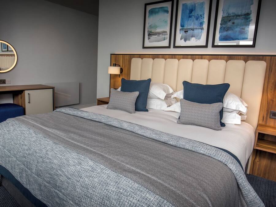 A hotel room with a bed, bedside tables, a desk, a mirror, and artwork on the wall.