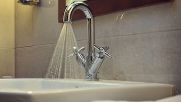Un lavandino in bagno con rubinetteria cromata e acqua corrente, uno specchio sopra e una pila di asciugamani bianchi.
