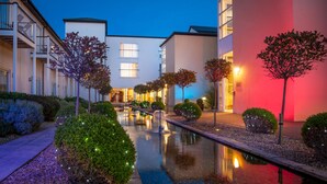 A modern hotel courtyard with a reflective water feature, neatly trimmed hedges, and illuminated trees. - Quay Hotel and Spa (Conwy)