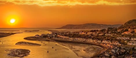 A coastal town at sunset with boats in the water, a pier, and buildings along the shore.