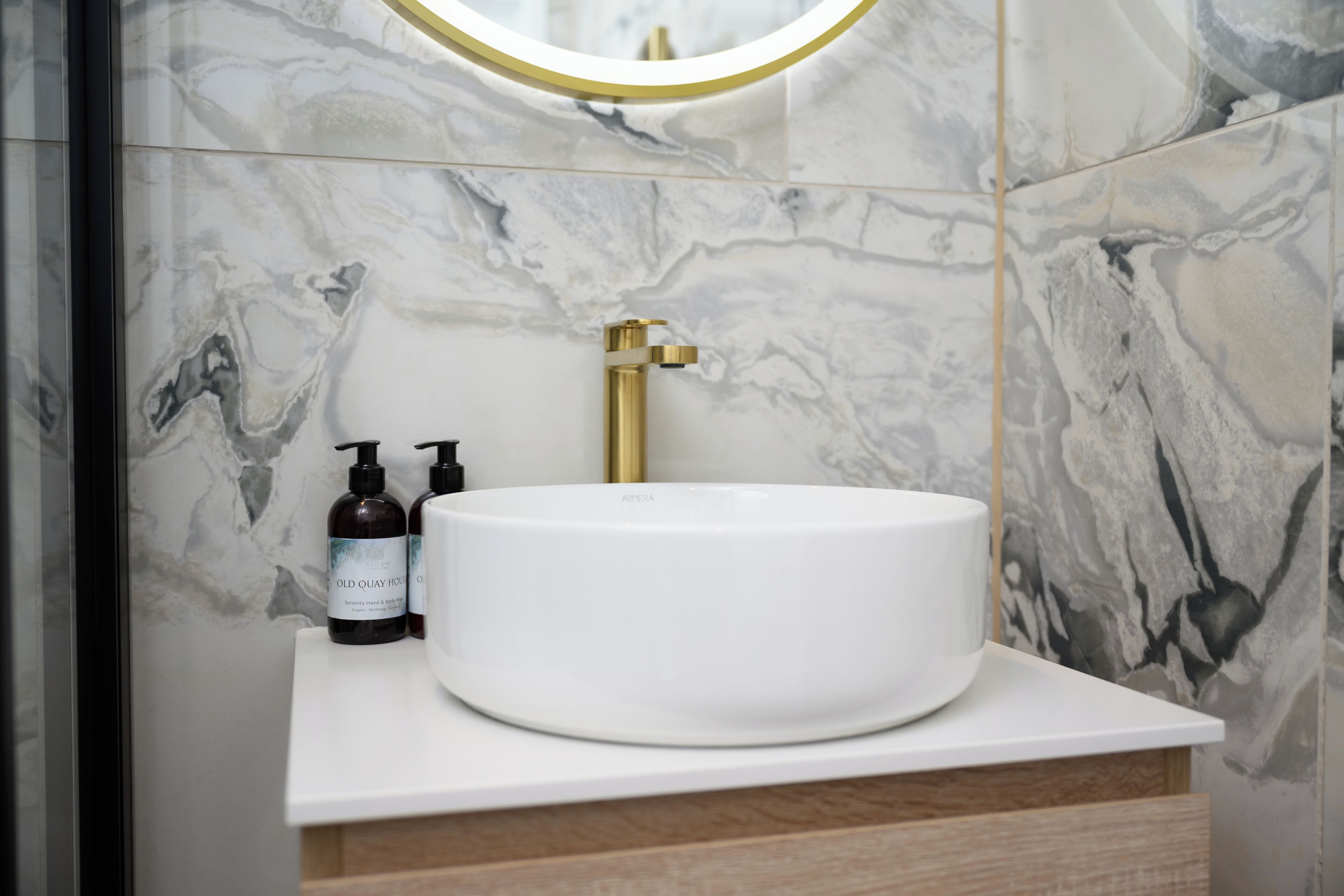 A bathroom with a marble wall, a white sink, and two bottles of hand soap.