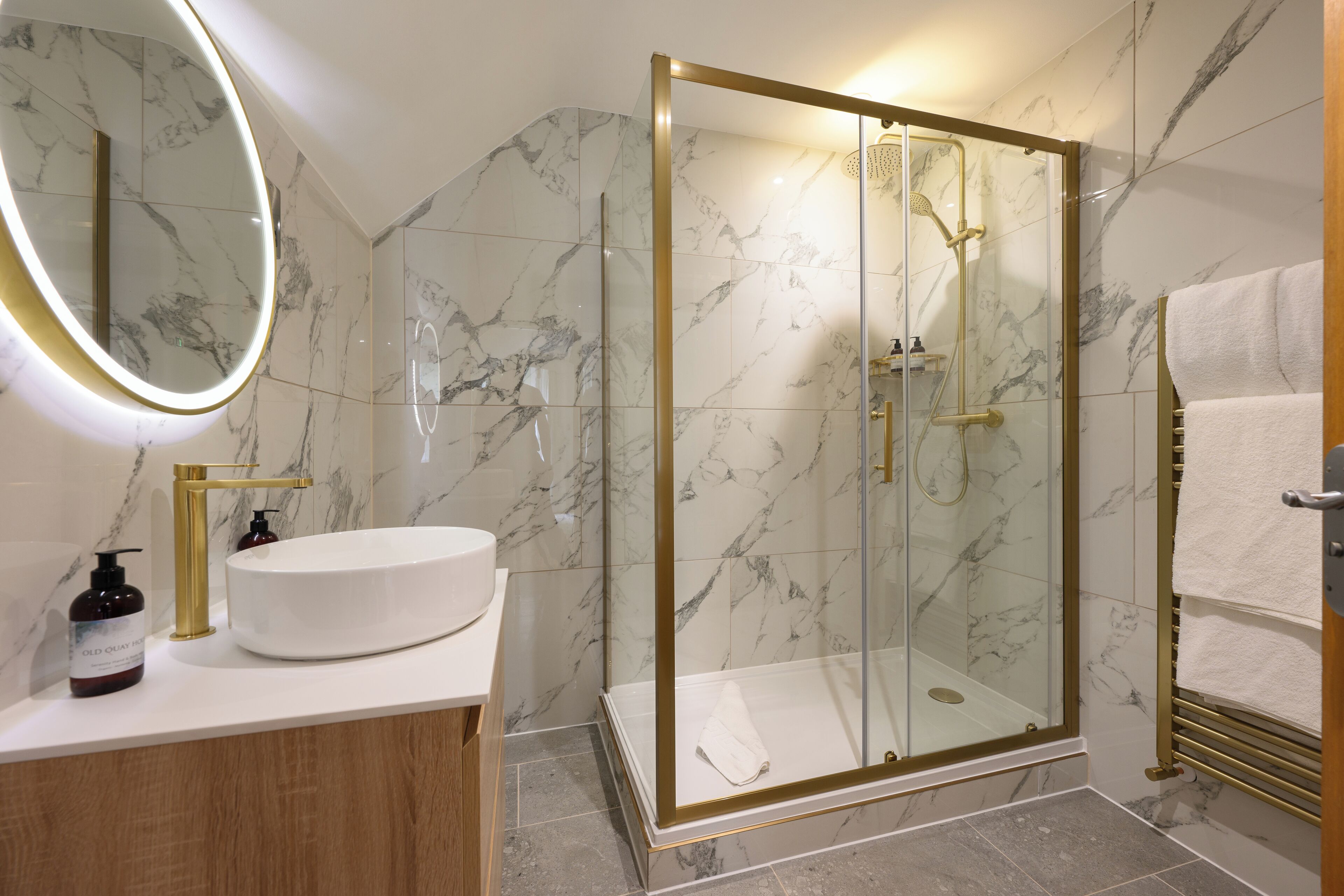 Ein modernes Badezimmer mit einer in Glas eingefassten Dusche, einer Marmorfliesenwand, einem runden Spiegel und einem hölzernen Waschtisch.